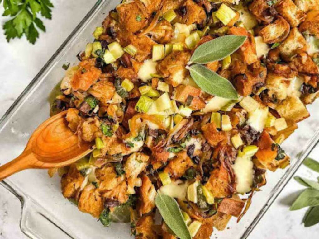 A glass baking dish filled with a mixture of baked bread cubes, herbs, and vegetables, with fresh sage leaves.