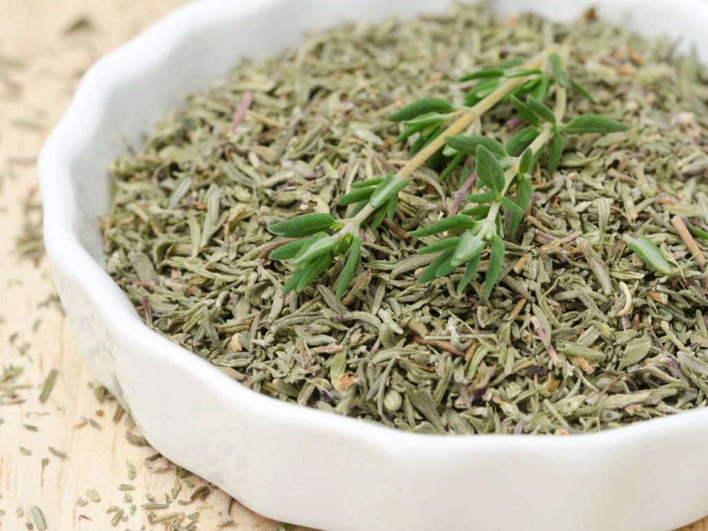 A white bowl filled with dried, finely chopped green herb leaves.