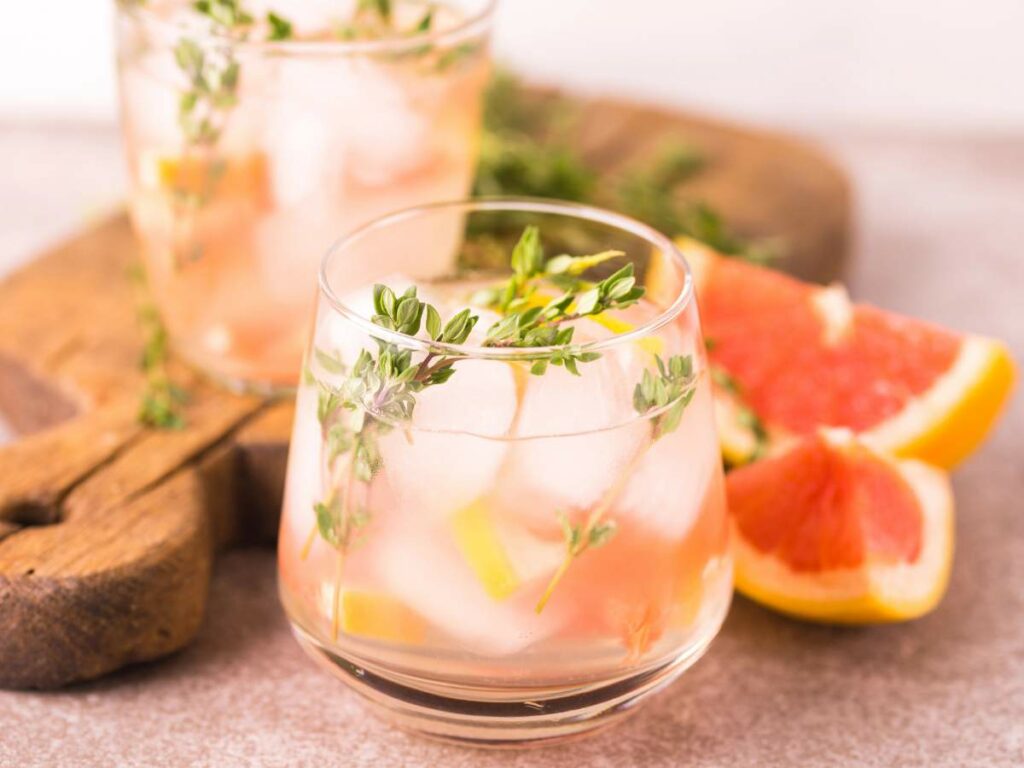 Two glasses of a pink beverage with ice cubes, garnished with thyme sprigs.