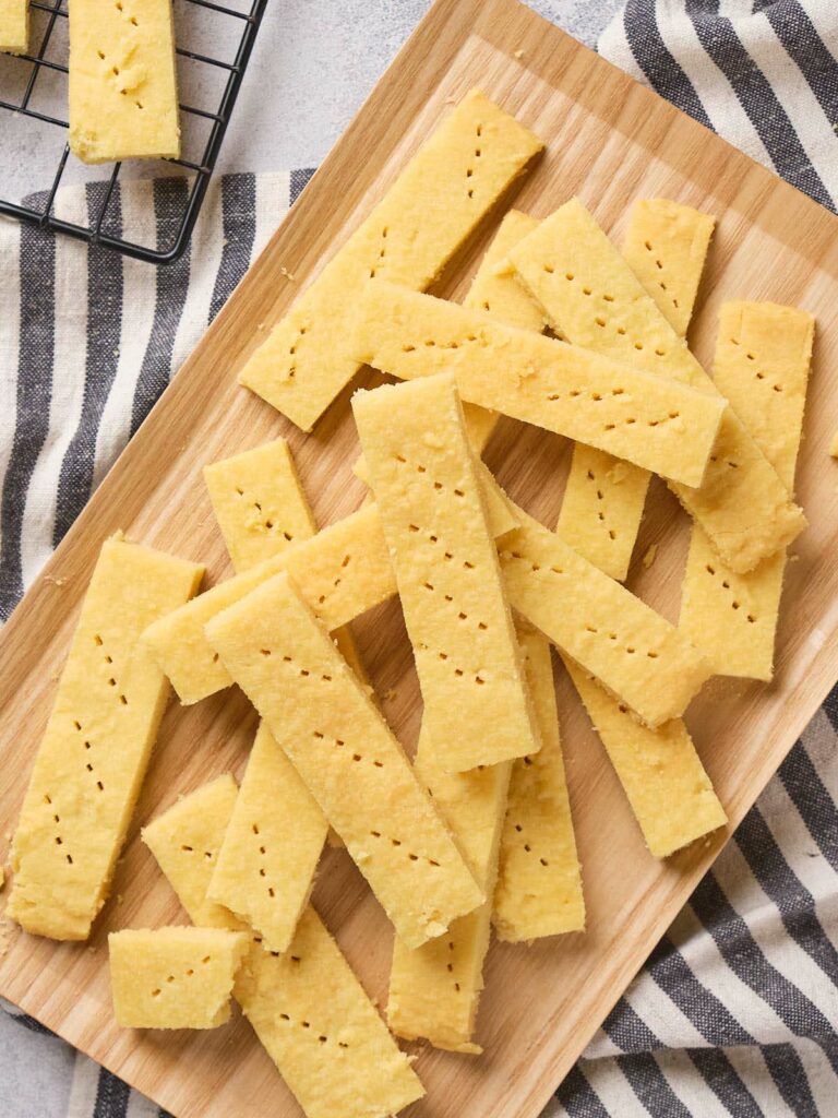 Golden shortbread cookies are arranged on a wooden board, with a striped cloth underneath.