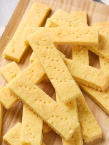 A stack of rectangular, golden yellow shortbread cookies are placed on a wooden surface.