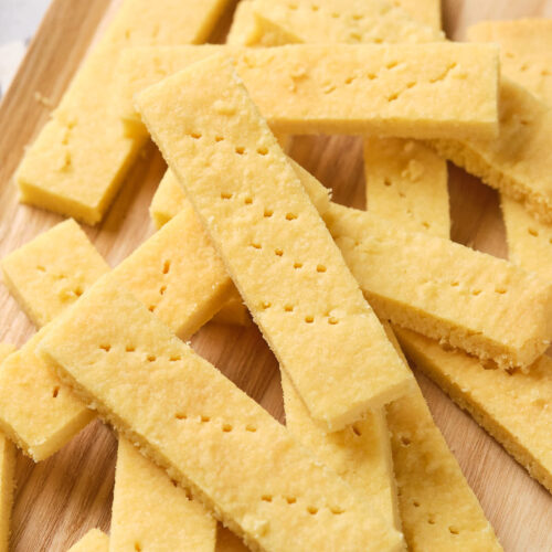 A stack of rectangular, golden yellow shortbread cookies are placed on a wooden surface.