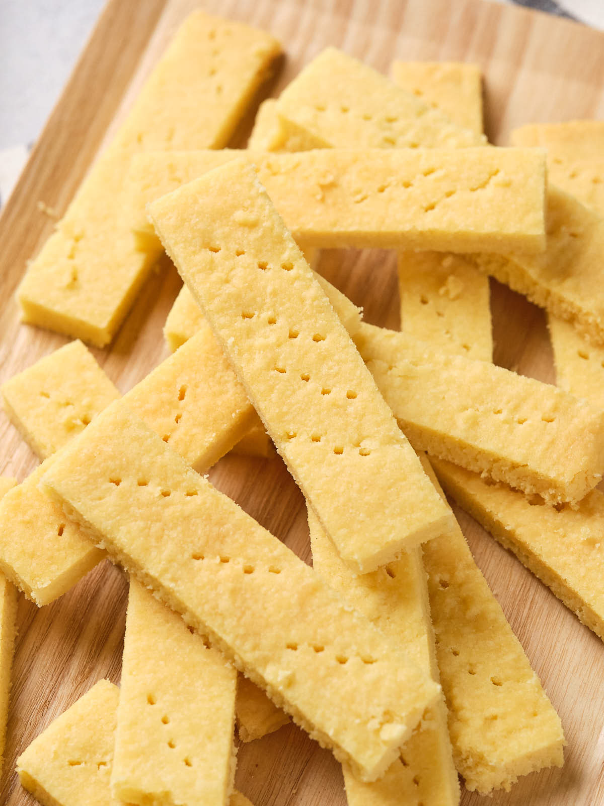 A stack of rectangular, golden yellow shortbread cookies are placed on a wooden surface.