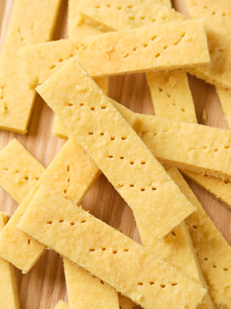 A pile of rectangular shortbread cookies with small holes on a wooden surface.