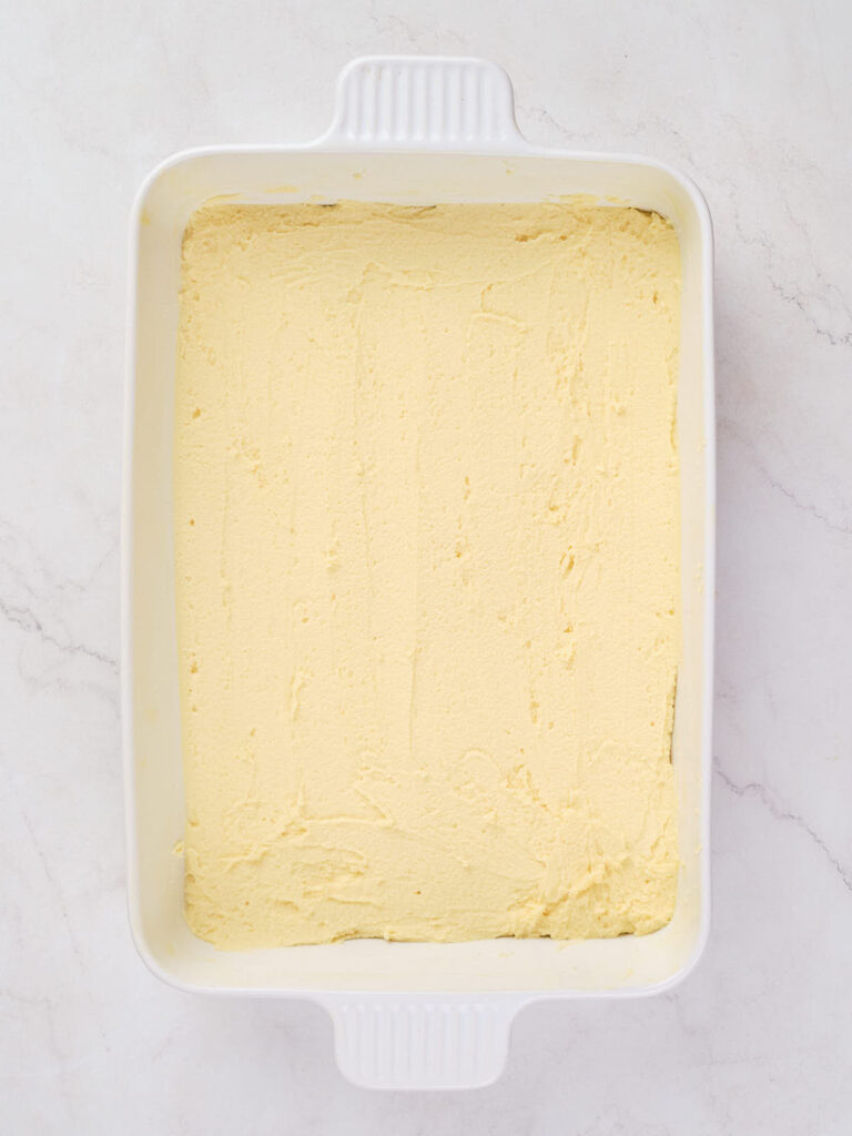 A rectangular white baking dish filled with smooth, evenly spread yellow batter on a light surface.