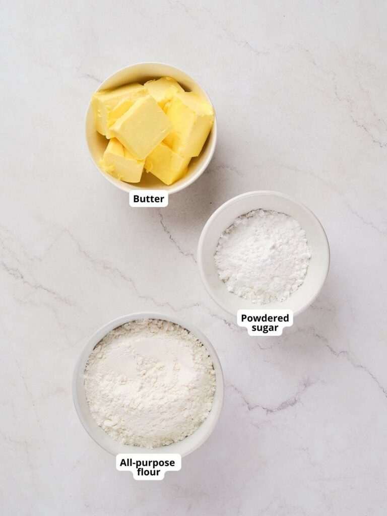 Three bowls on a marble surface containing butter, powdered sugar, and all-purpose flour.