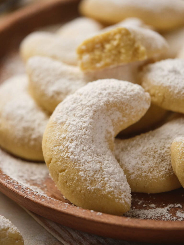 A plate of crescent-shaped cookies dusted with powdered sugar, with one cookie missing a bite.