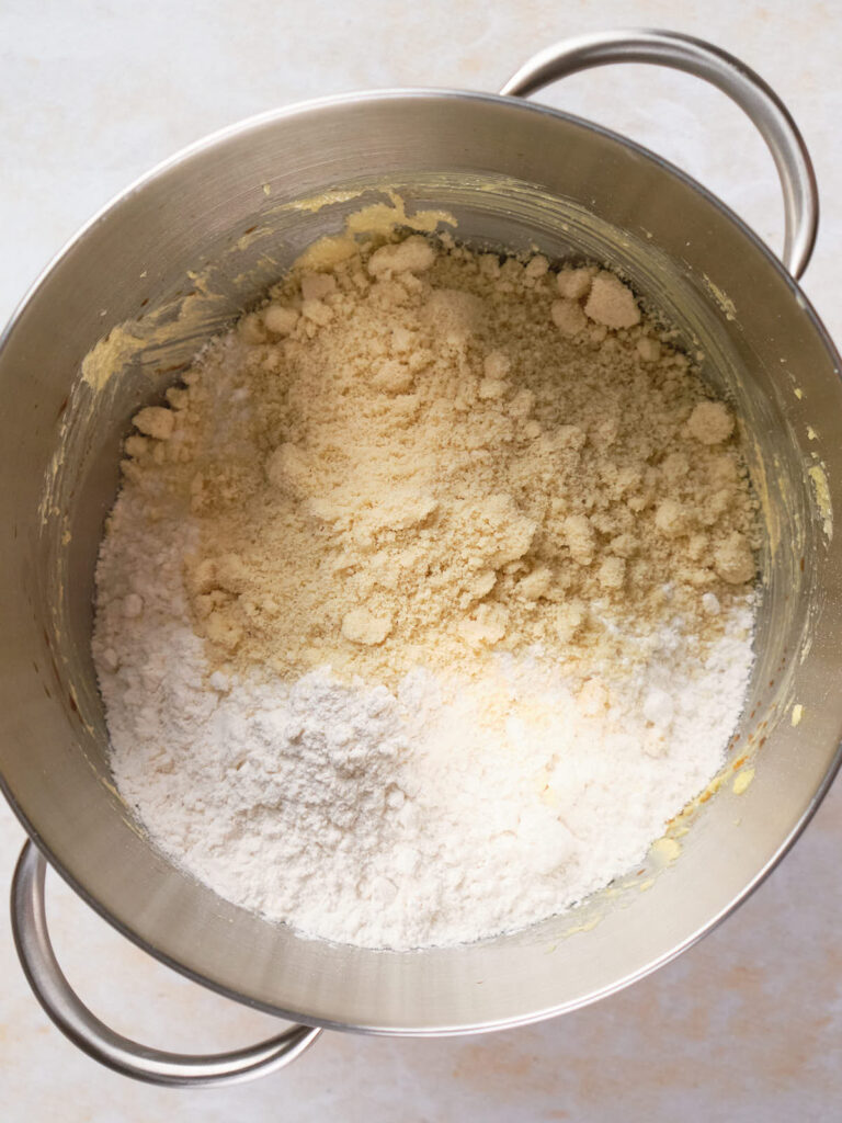 A metal mixing bowl containing almond flour, sugar, and other baking ingredients.