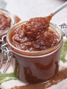 A jar of thick, brown apple butter with a spoon scooping some out.