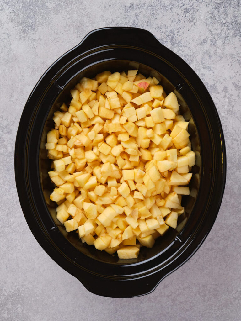 Diced apples in a black slow cooker on a gray textured surface.