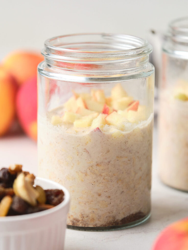 A glass jar containing apple cinnamon overnight oats topped with diced apple pieces.