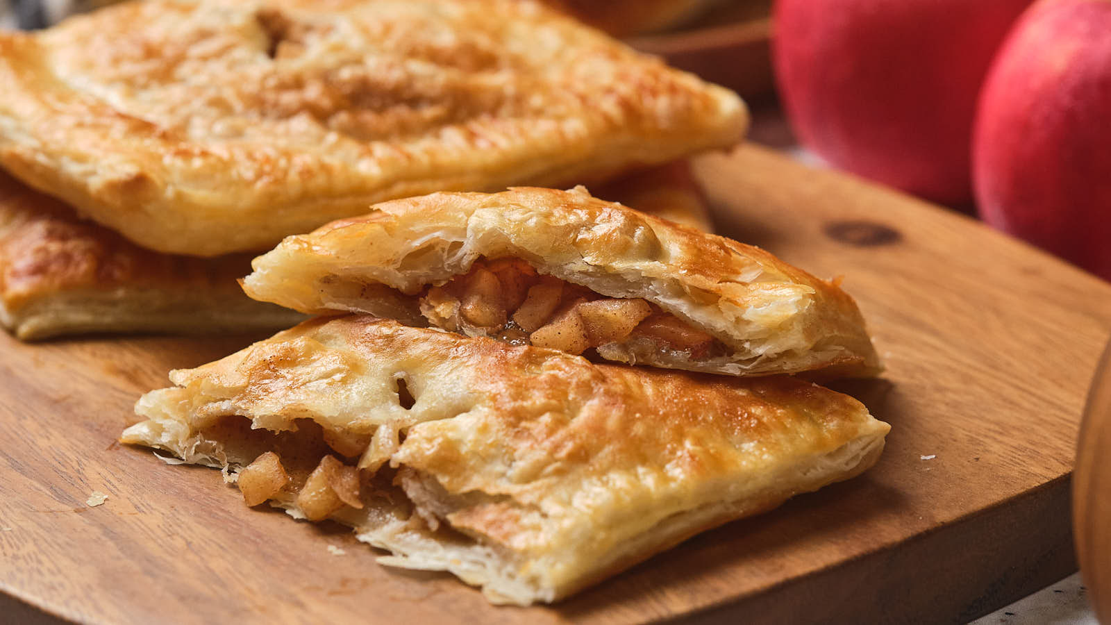 A flaky pastry filled with spiced apples is cut in half on a wooden board.