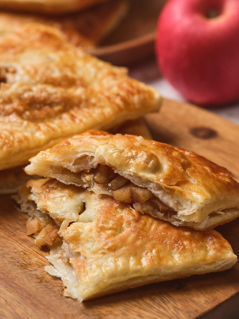 Golden brown apple pie cut in half, showing apple filling, on a wooden surface.