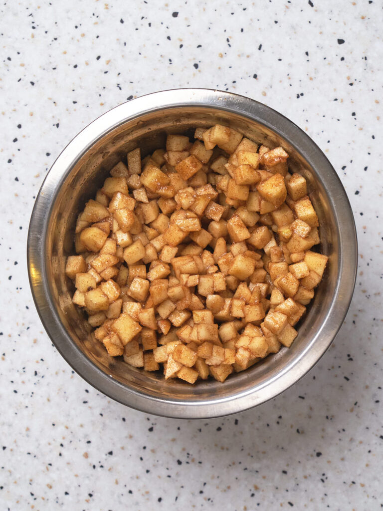 Diced apples in a mixing bowl covered in sugar.