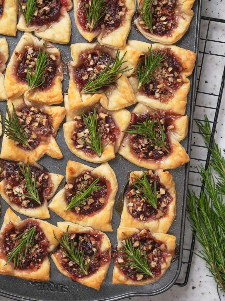 Brie bites topped with fresh rosemary, arranged on a baking tray.