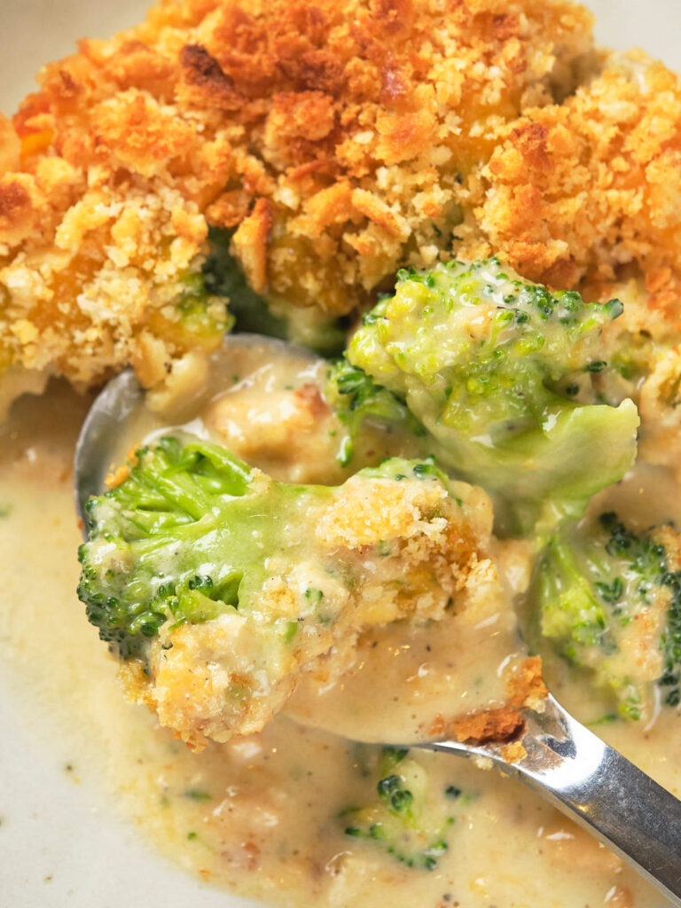 A spoonful of broccoli casserole with a crispy breadcrumb topping on a plate.