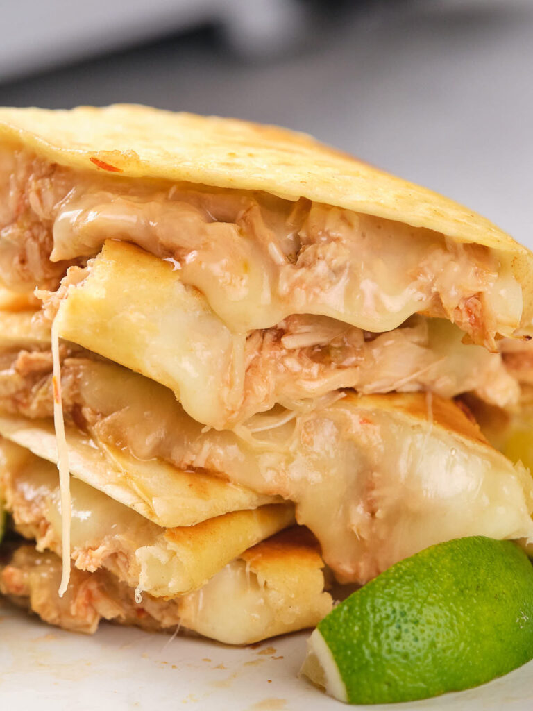 Close-up of a stack of cheesy chicken quesadillas with a lime wedge on the side.