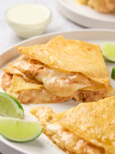 Close-up of cheesy chicken quesadillas served on a white plate with lime wedges.