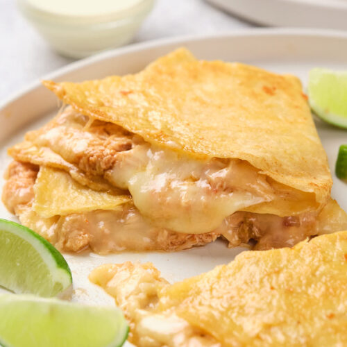 Close-up of cheesy chicken quesadillas served on a white plate with lime wedges.