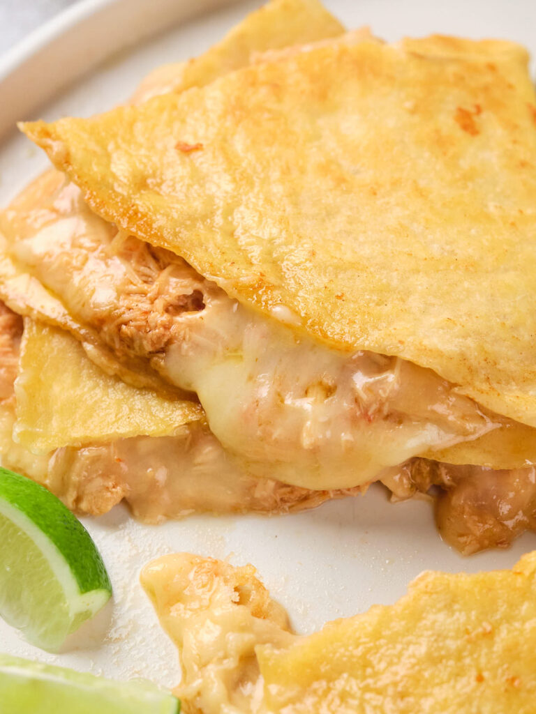 Close-up of a quesadilla with melted cheese and shredded meat, served with lime wedges.