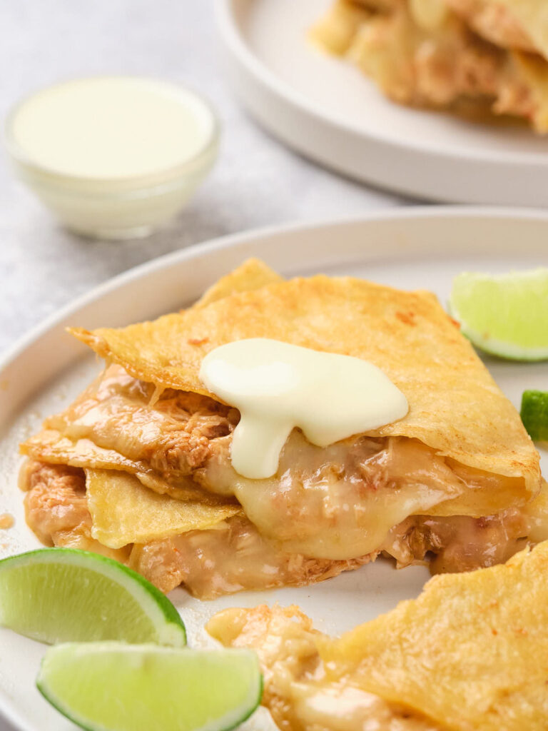 A plate of cheesy quesadillas with chicken, topped with a dollop of white sauce.