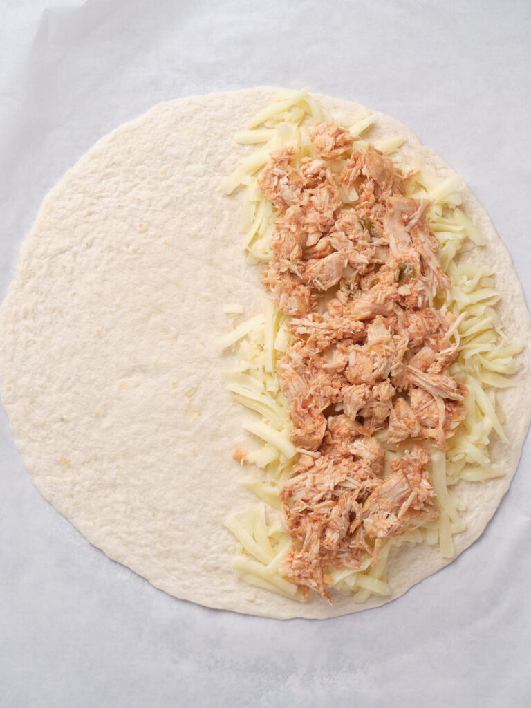 Tortilla topped with shredded cheese and shredded chicken, ready to be folded.