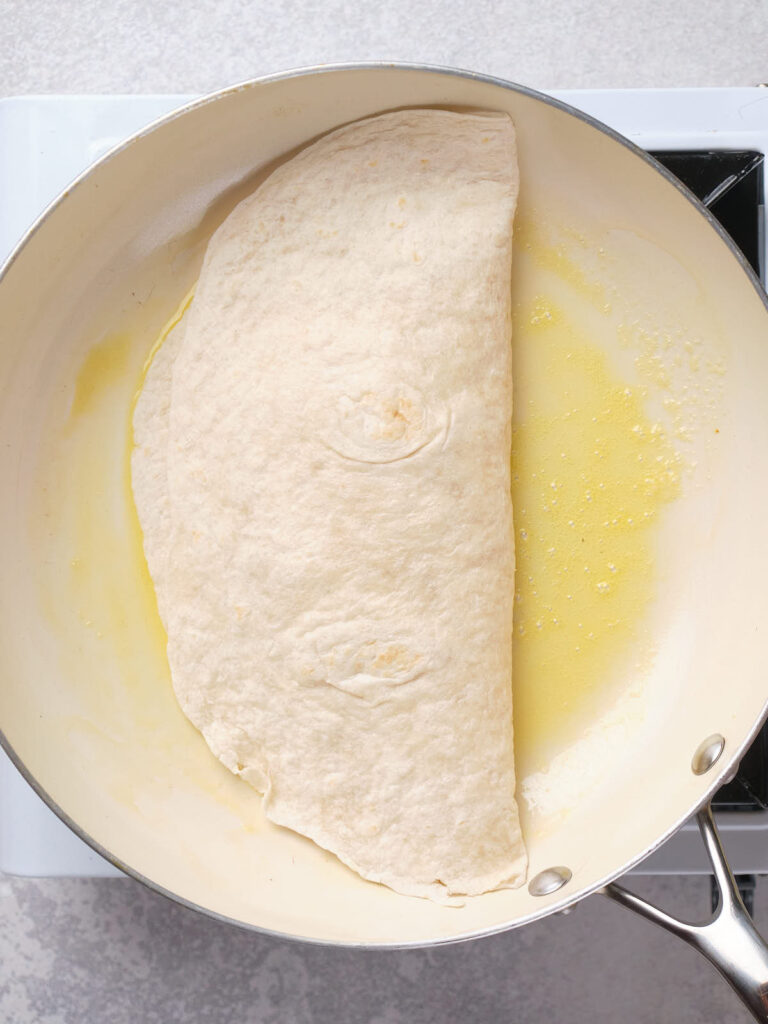 A folded tortilla cooking in a pan with melted butter.