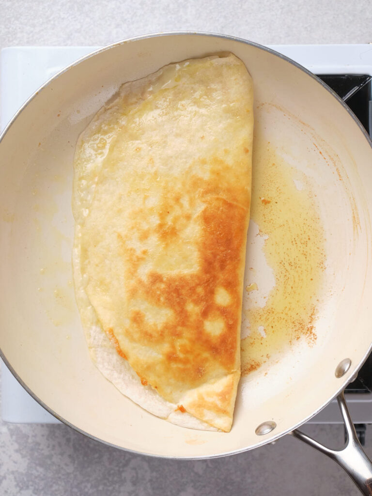 A quesadilla is half-folded and being cooked in a pan on a stove.