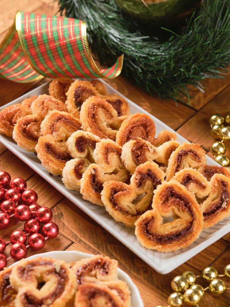 A plate of cinnamon palmiers is on a wooden table.