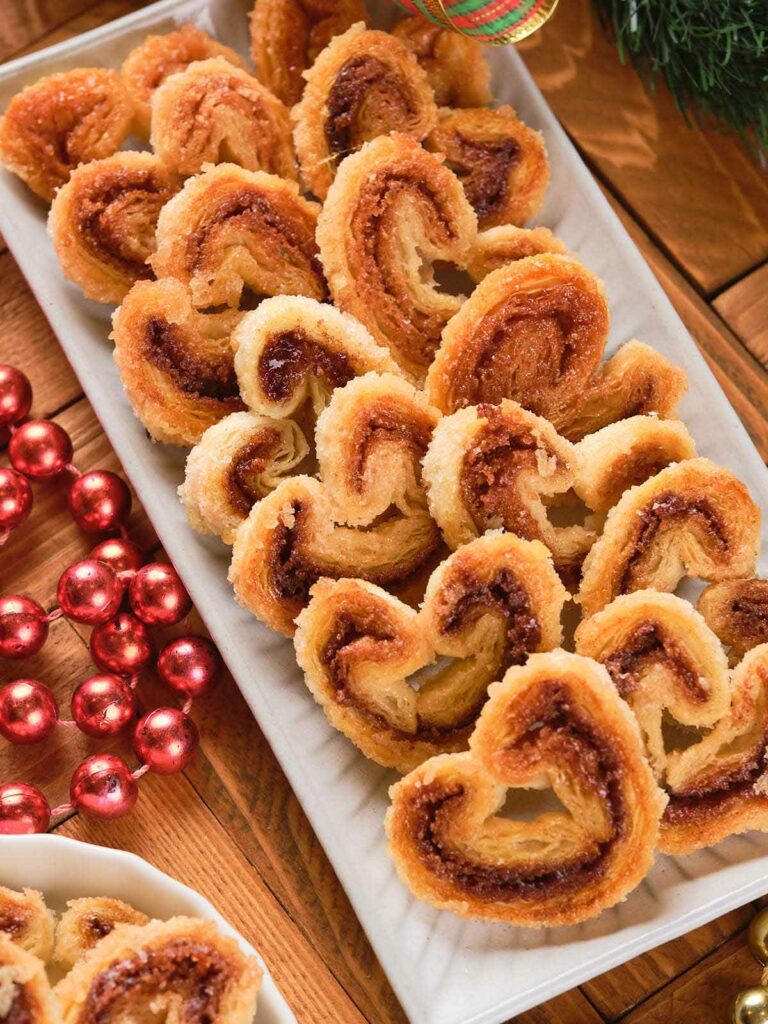 A rectangular platter with neatly arranged cinnamon palmiers, placed on a wooden table.