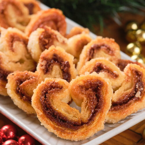 A plate of cinnamon palmiers arranged neatly on a table with red and gold decorations.