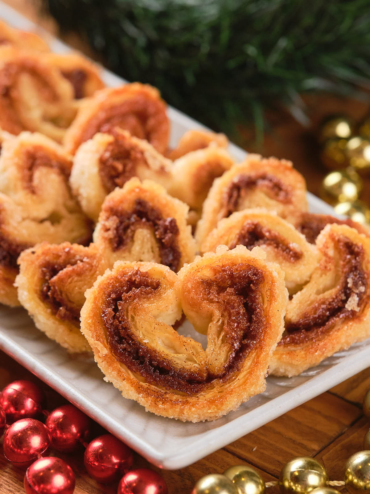 A plate of cinnamon palmiers arranged neatly on a table with red and gold decorations.