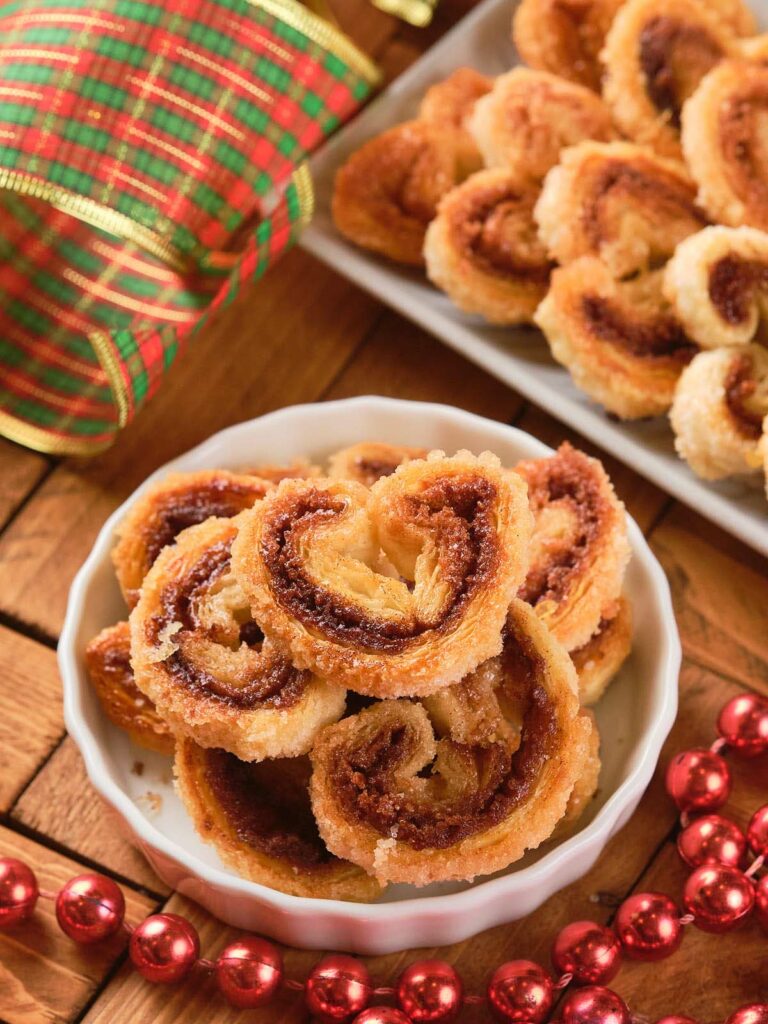 A bowl of cinnamon palmiers on a wooden surface.