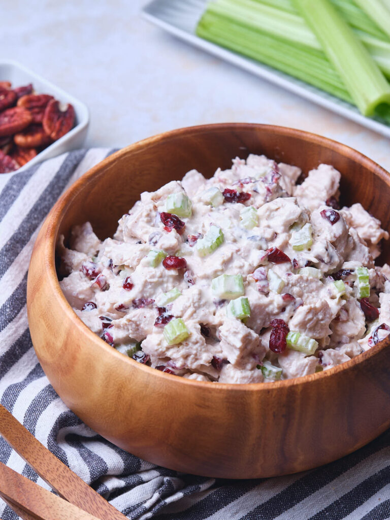 A wooden bowl filled with cranberry chicken salad placed on a striped cloth.