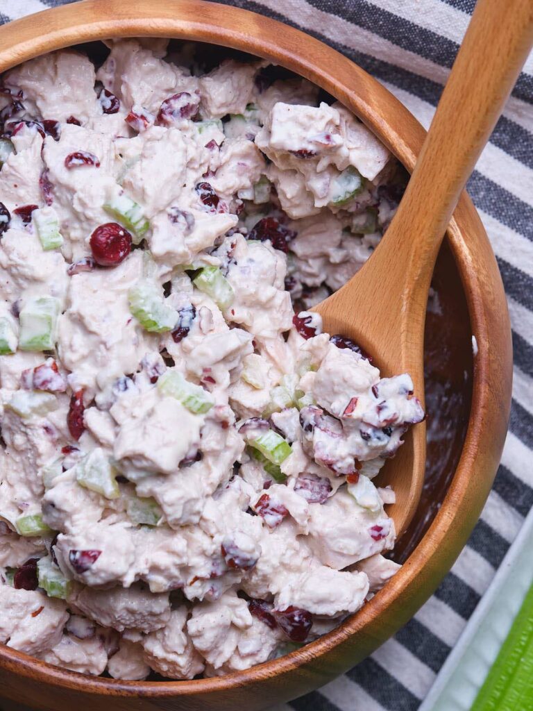 A wooden bowl filled with cranberry chicken salad mixed with celery.