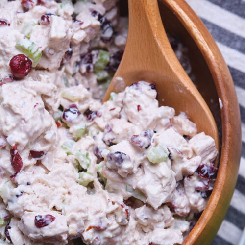 A wooden spoon in a bowl of cranberry chicken salad with chopped celery.