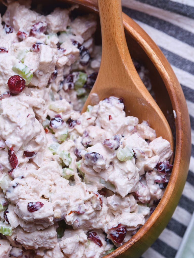 A wooden spoon in a bowl of cranberry chicken salad with chopped celery.