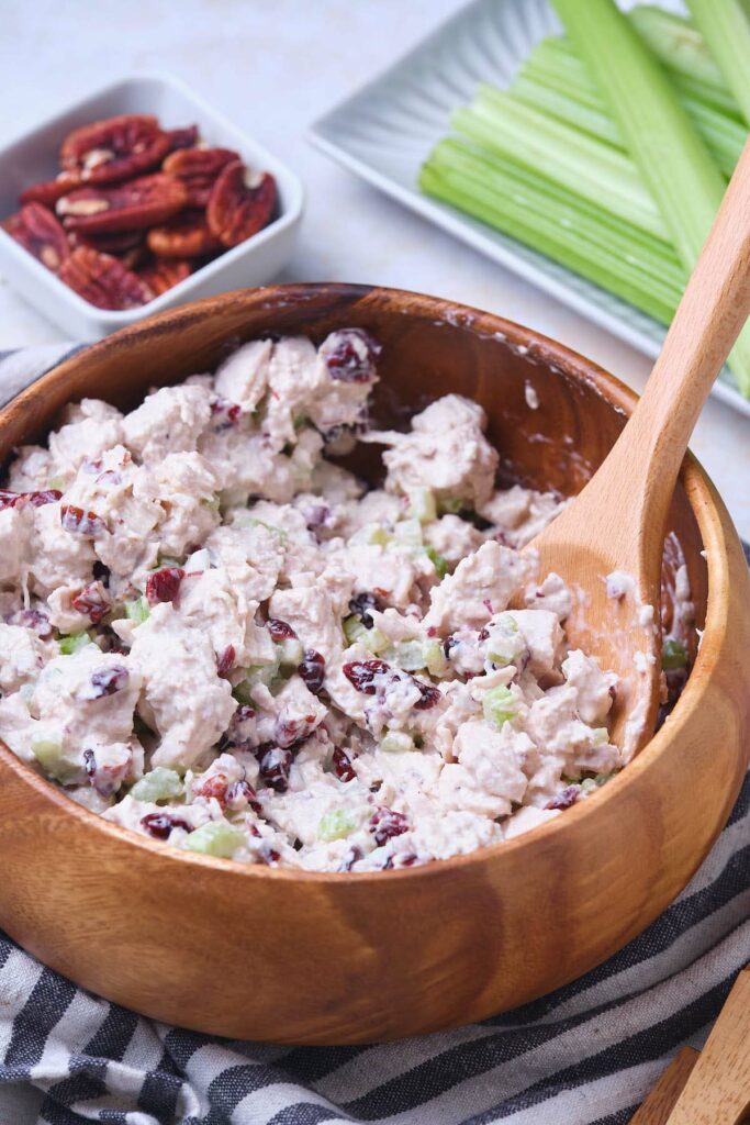 A wooden bowl filled with cranberry chicken salad, a wooden spoon inside.