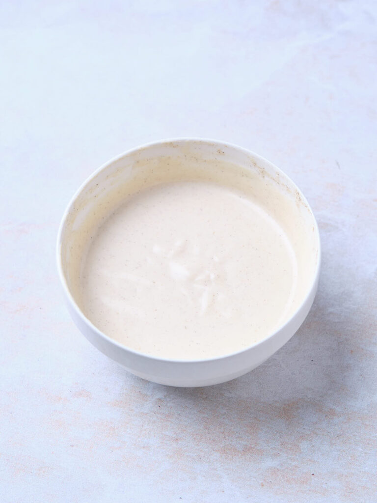 A white bowl filled with a creamy, off-white dressing placed on a light surface.