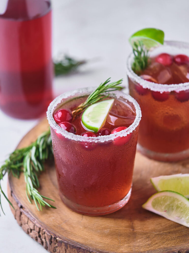 Two glasses of cranberry margarita placed on a wooden board.