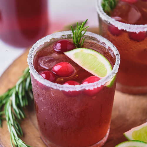 Two glasses of cranberry margarita on a wooden platter.