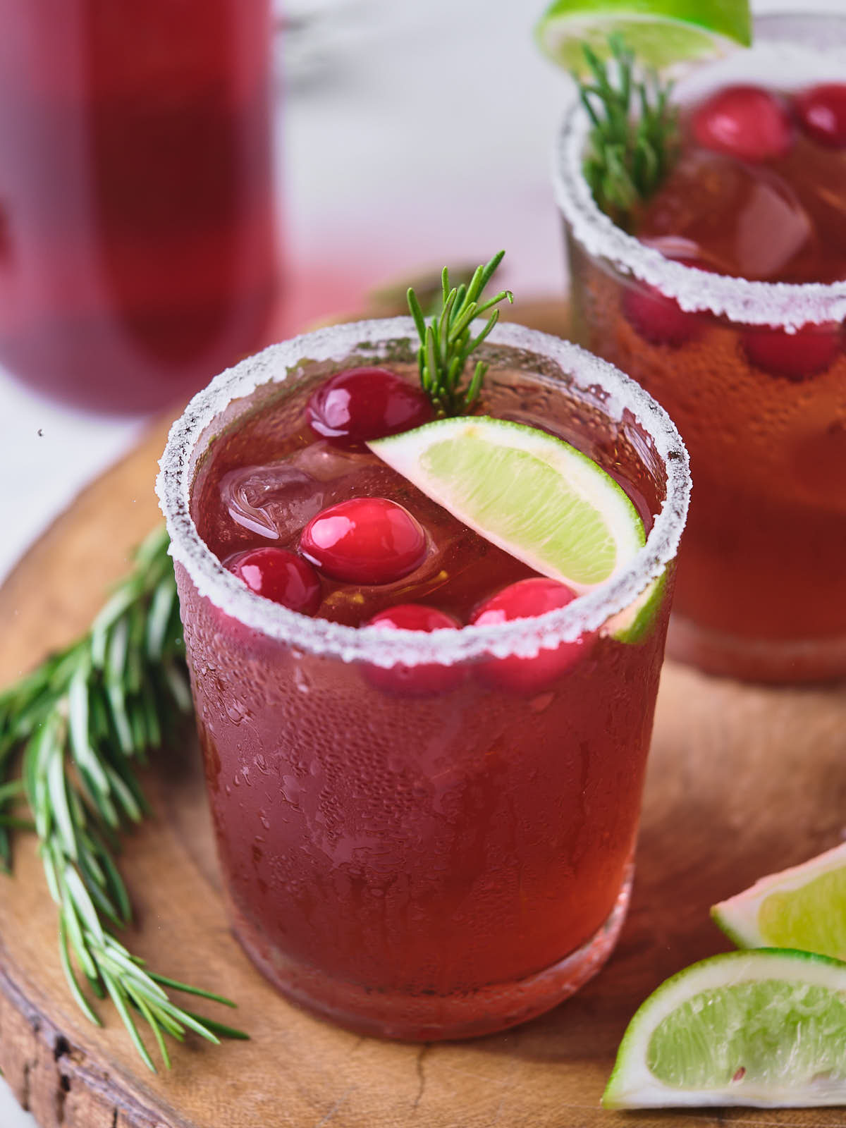 Two glasses of cranberry margarita on a wooden platter.