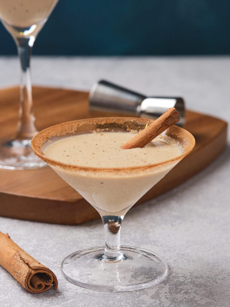 Eggnog martini in a glass, garnished with a cinnamon stick and rimmed with cinnamon sugar.