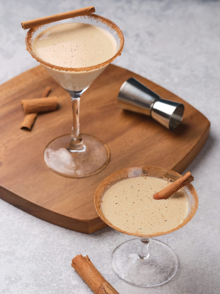 Two glasses filled with eggnog martini, each garnished with a cinnamon stick.