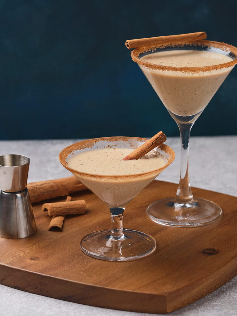 Two glasses filled with eggnog martini, garnished with cinnamon sticks.