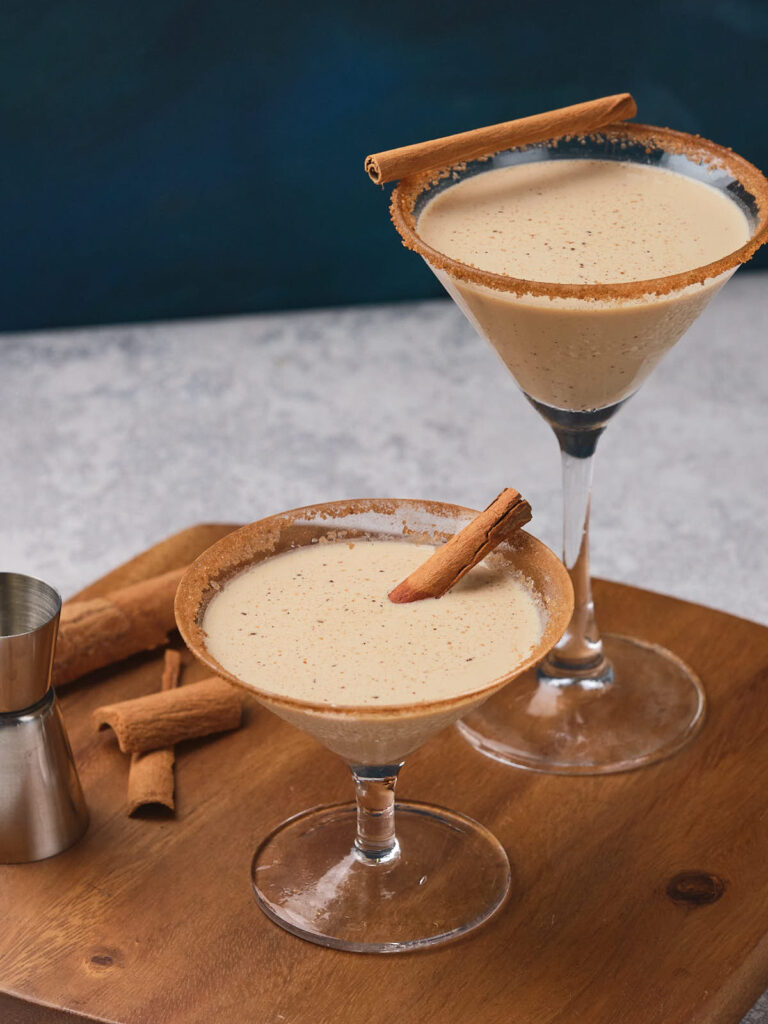 Two glasses filled with eggnog martini placed on a wooden surface.