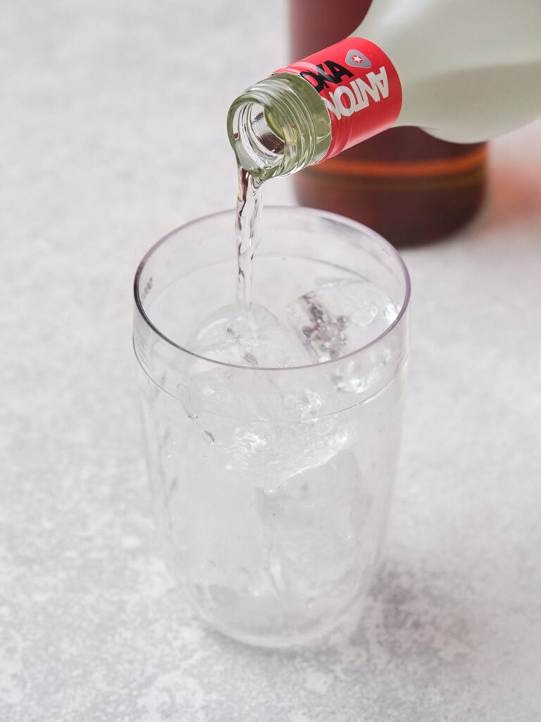 A clear liquid is being poured into a glass filled with ice cubes.