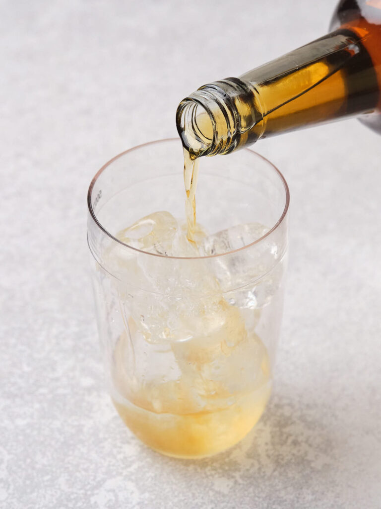 A brown beverage is being poured from a bottle into a glass filled with ice cubes.