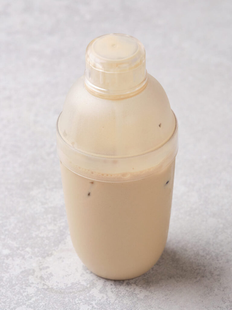 Plastic shaker bottle filled with iced coffee on a gray surface.