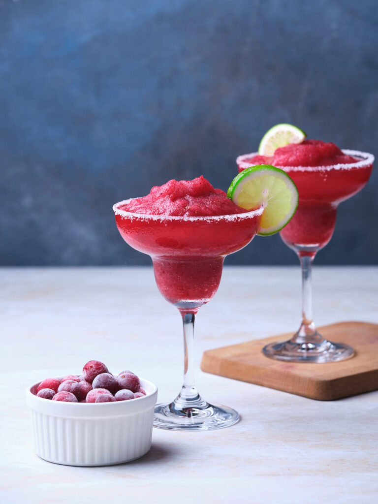 Two glasses of frozen cranberry margarita with lime slices on the rims.